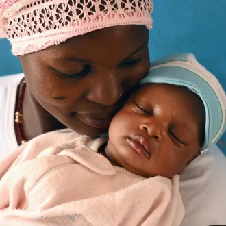 Mother resting her cheek on her sleeping newborn's head at a health centre.