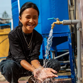 Girl smiling and catching water from an outdoor tap with her hands.
