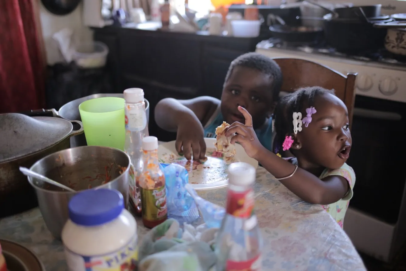 Alishia (right) and her cousin, KJ, eat a snack at their grandmother’s home, in Belize City. 
