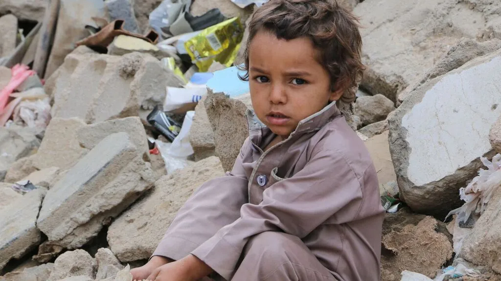 Yemeni child beside destroyed house