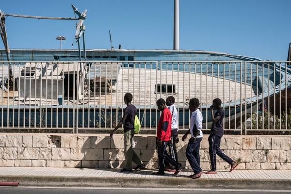 the crew walks past a smuggler's boat in Sicily