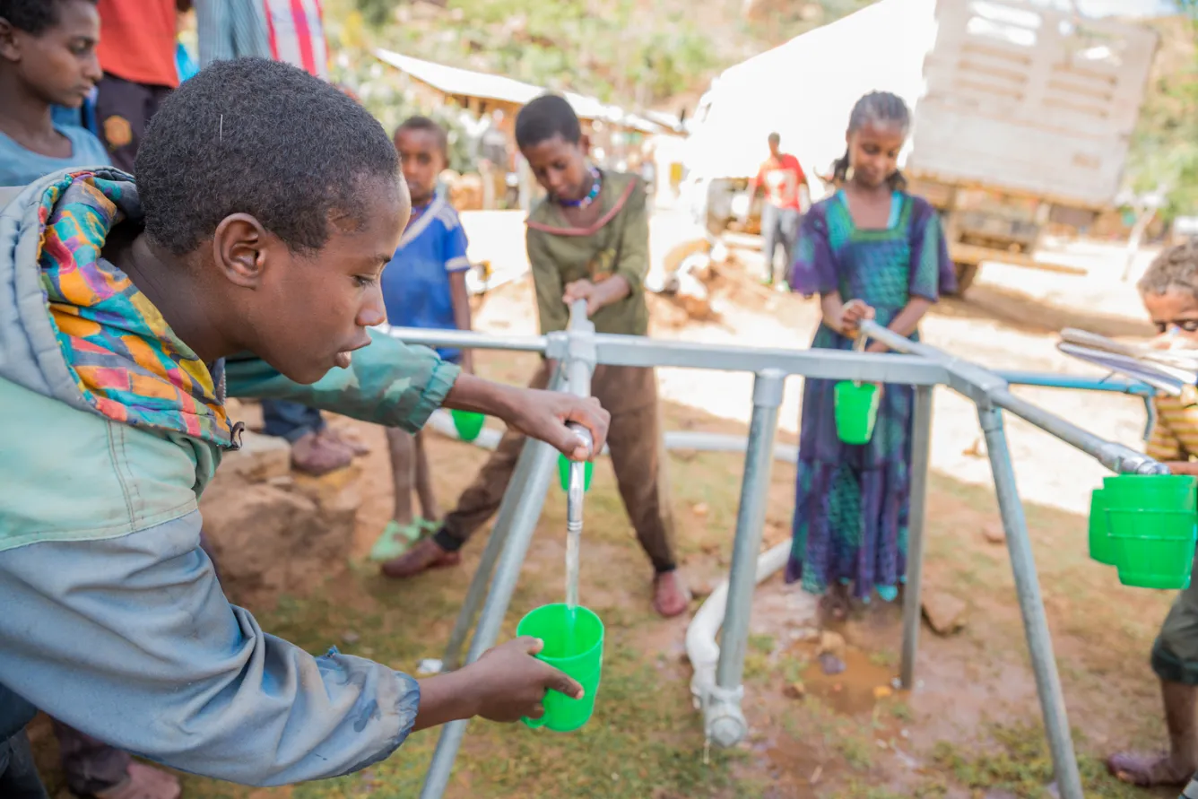 Students fill their drinking cups from a tap connected to a water bladder installed by UNICEF .