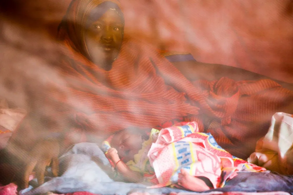 A woman sits with her newborn under a mosquito net