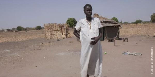 Nyibol who lives in South Sudan holds her pregnant belly outside her hut.