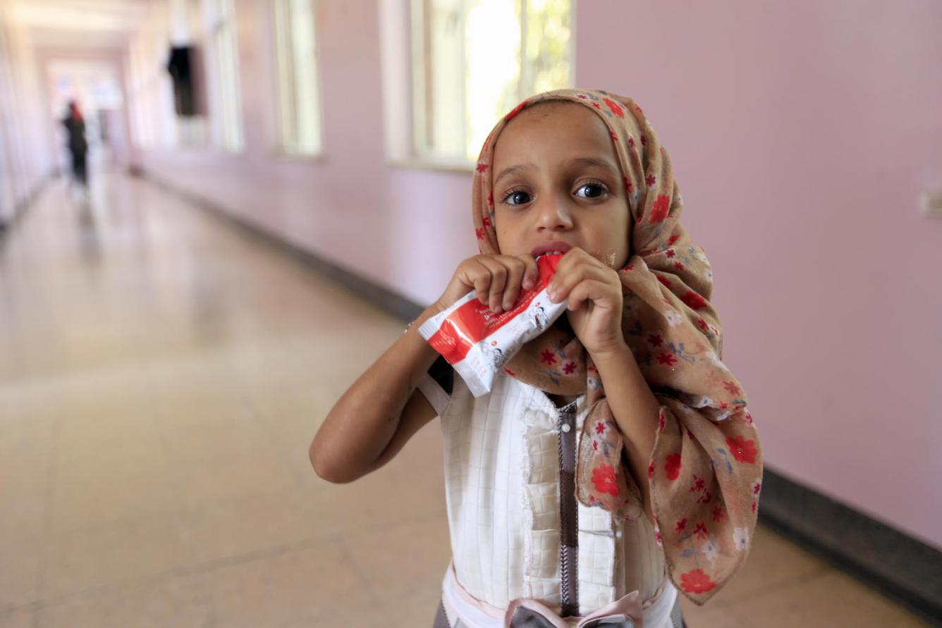 A small girl eats nutrient- and protein-rich Plumpy’Nut® paste while being treated for malnutrition at a hospital in Saana.