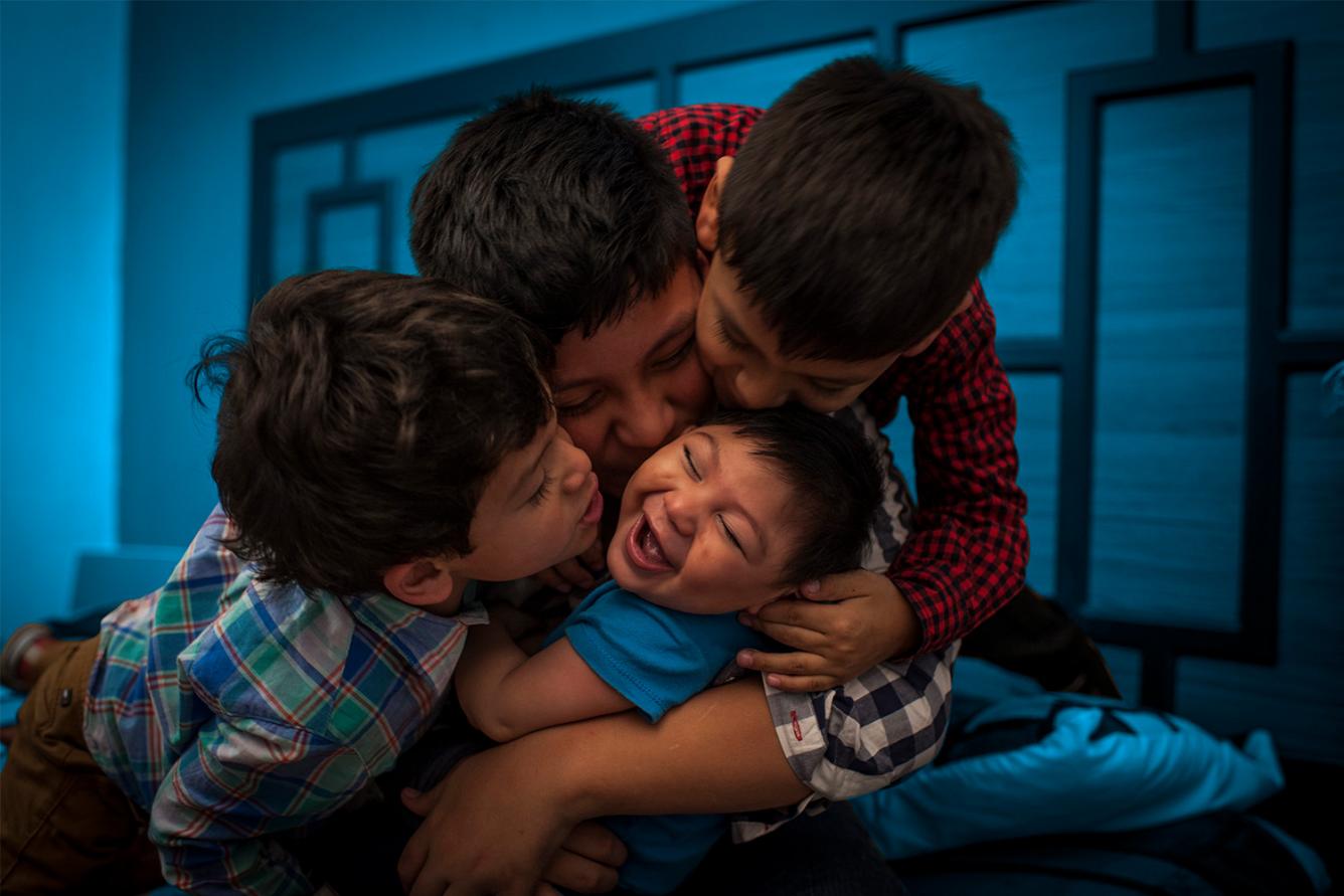 A toddler boy laughs as he is hugged by his friends. Convention on the Rights of the Child - 30th anniversary.