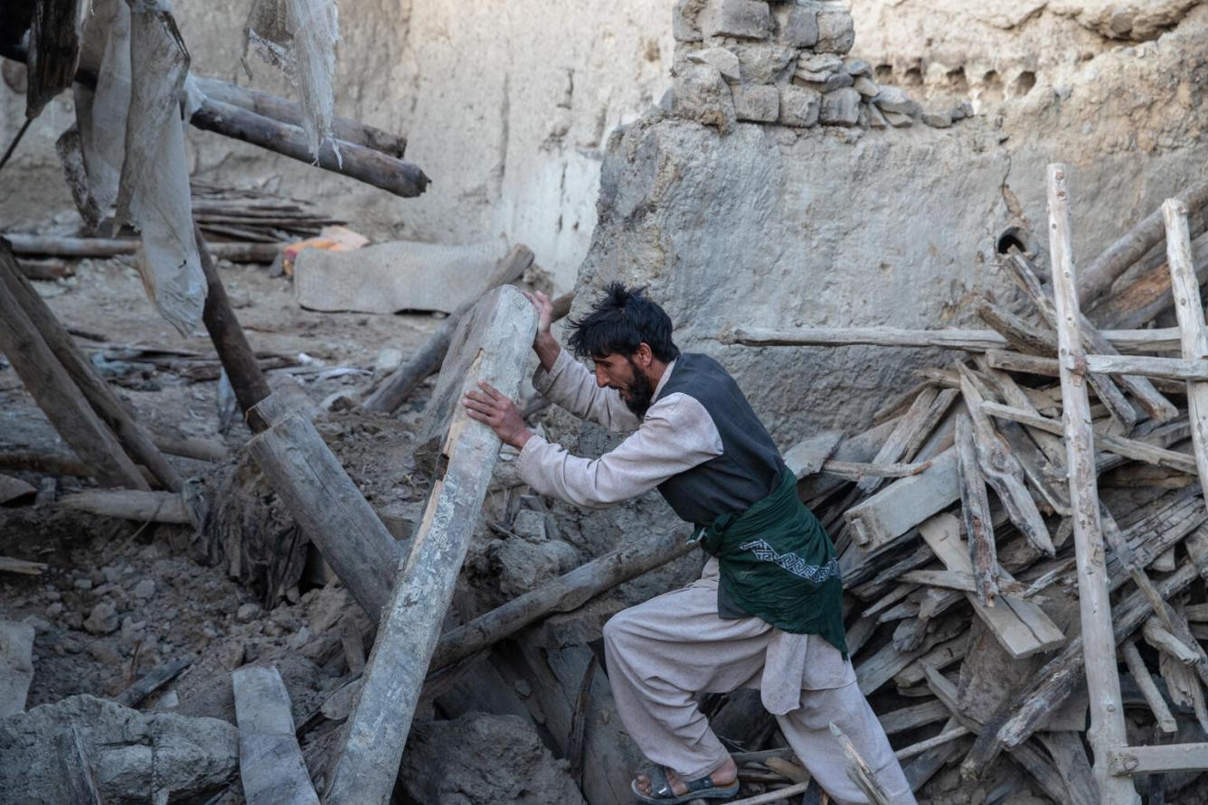 A man pushes a wooden column up in the rubble of a home
