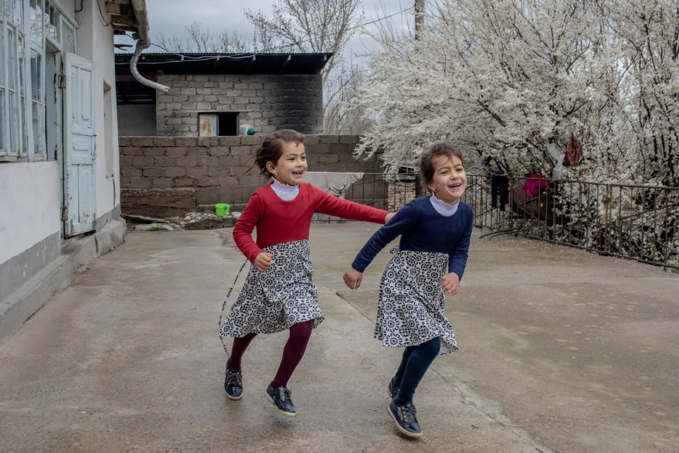 Les jumelles Magfirat et Marifat jouent à l’extérieur de leur maison dans le district de Vahdat au Tadjikistan.