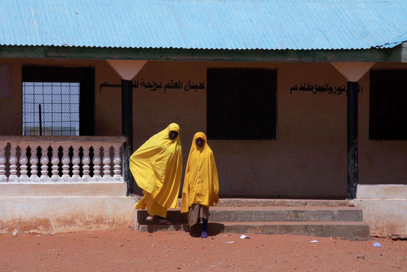 Two girls in yellow uniforms exit a school walking down some steps.