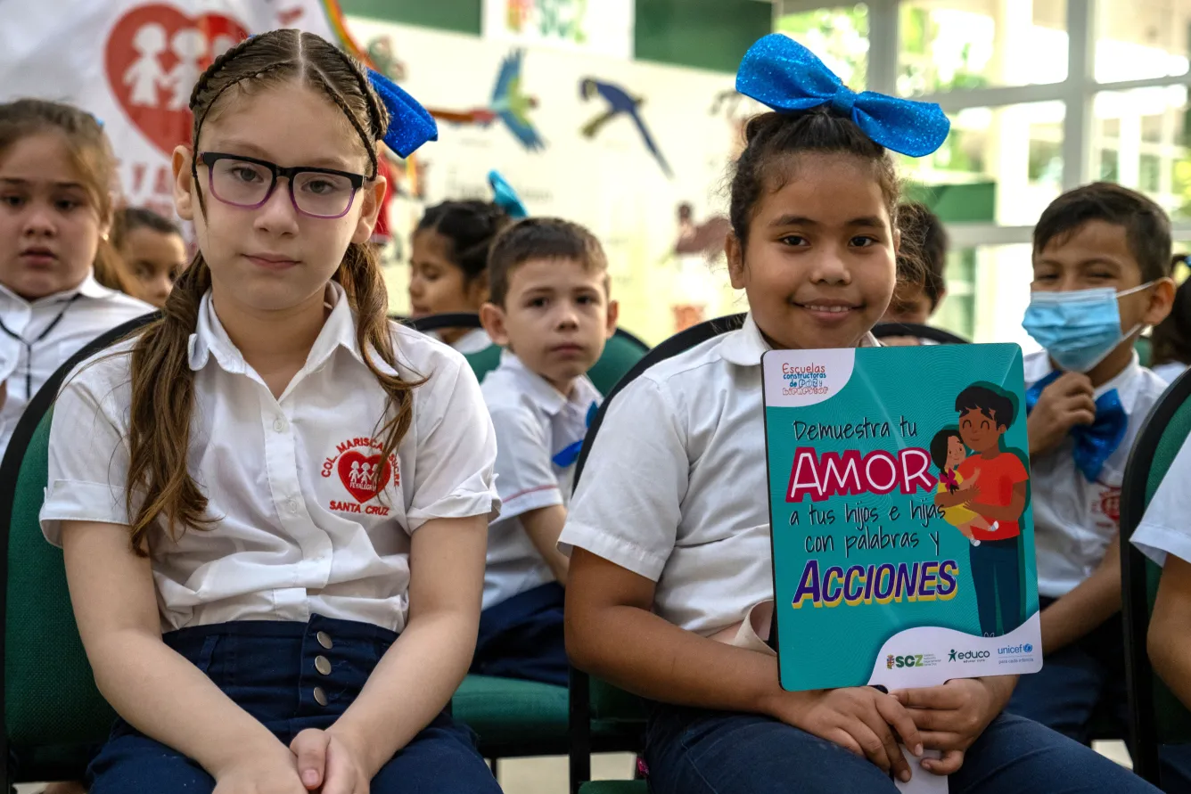 Deux jeunes filles en uniforme assises dans un auditorium lors d’une cérémonie sur la prévention de la violence à l’encontre des enfants dans une école à Santa Cruz, en Bolivie. Les deux enfants regardent la caméra.