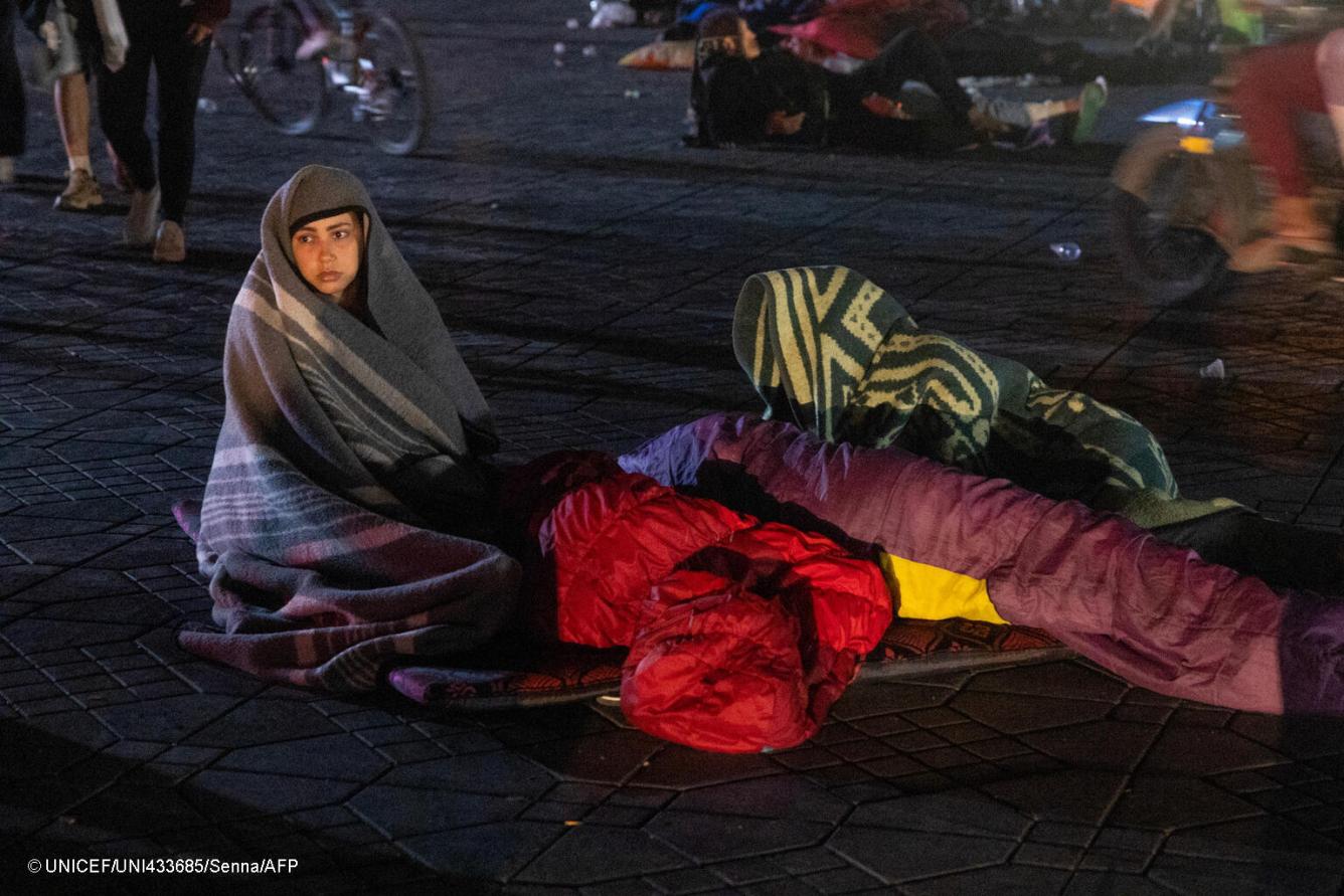 Une femme est assise, enveloppée dans une couverture lui couvrant la tête, tandis que d’autres habitants sont allongés sous des couvertures sur une place publique de Marrakech à la suite d’un séisme.