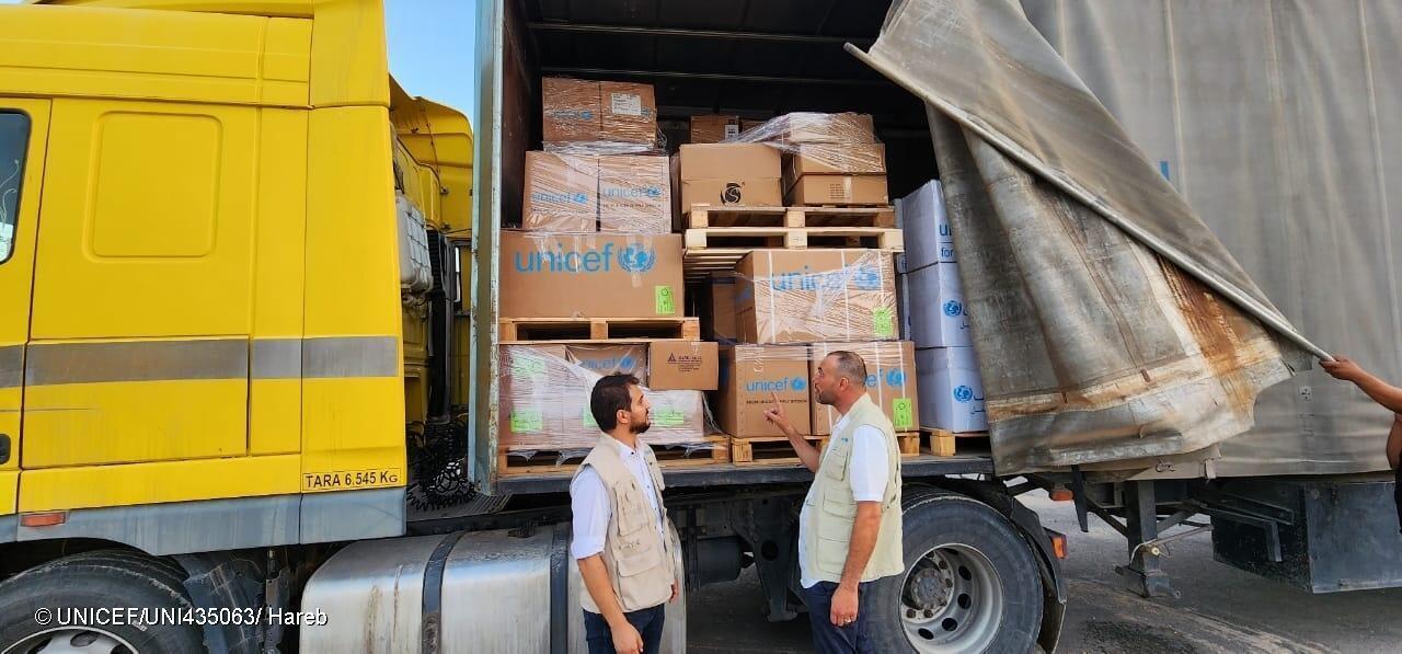 Deux hommes se tiennent debout près d’un camion chargé de boîtes à l’effigie de l’UNICEF.