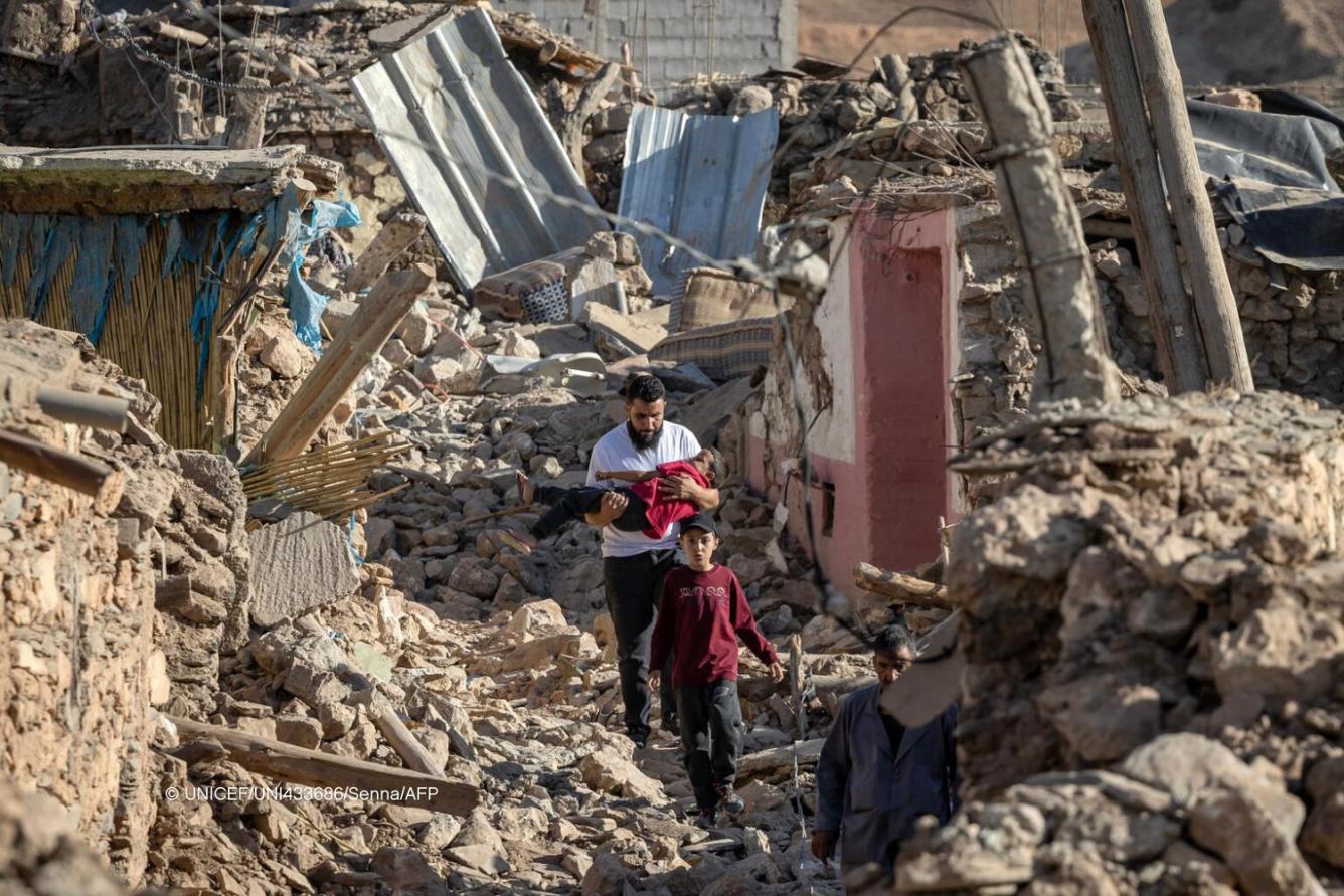 Un homme portant un enfant dans ses bras marche en compagnie d’un jeune garçon et d’un autre homme parmi les décombres de maisons effondrées à Marrakech à la suite d’un séisme.