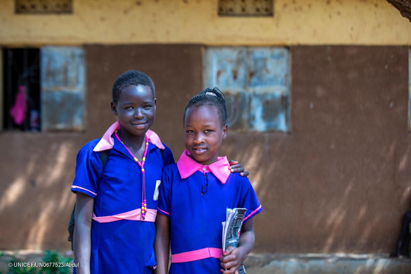 Deux filles en uniforme scolaire bleu se tiennent devant leur école.