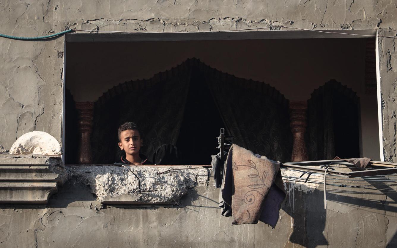 Un enfant regarde par la fenêtre d’un bâtiment endommagé.