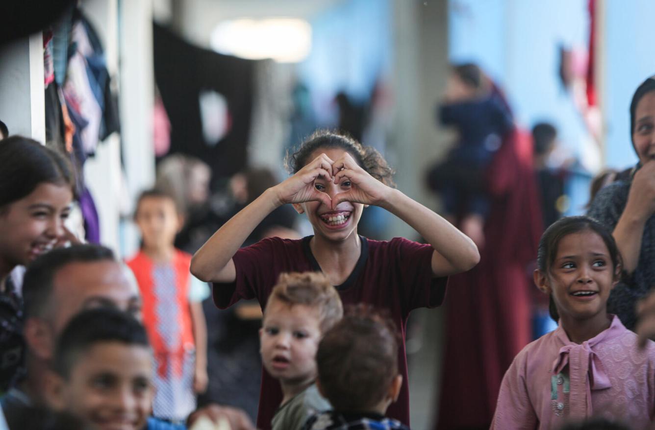 Une fille forme un cœur avec ses mains devant son visage. Autour d’elle, d’autres enfants regardent l’objectif.