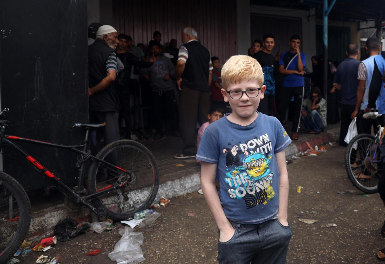 Un enfant, les mains dans les poches, regarde l’objectif. Derrière lui, des hommes en file attendent pour se procurer du pain.