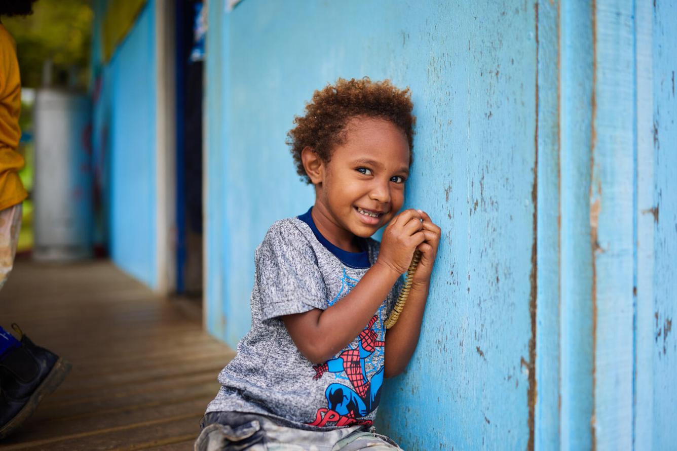 Un enfant appuyé contre un mur bleu regarde l’objectif.