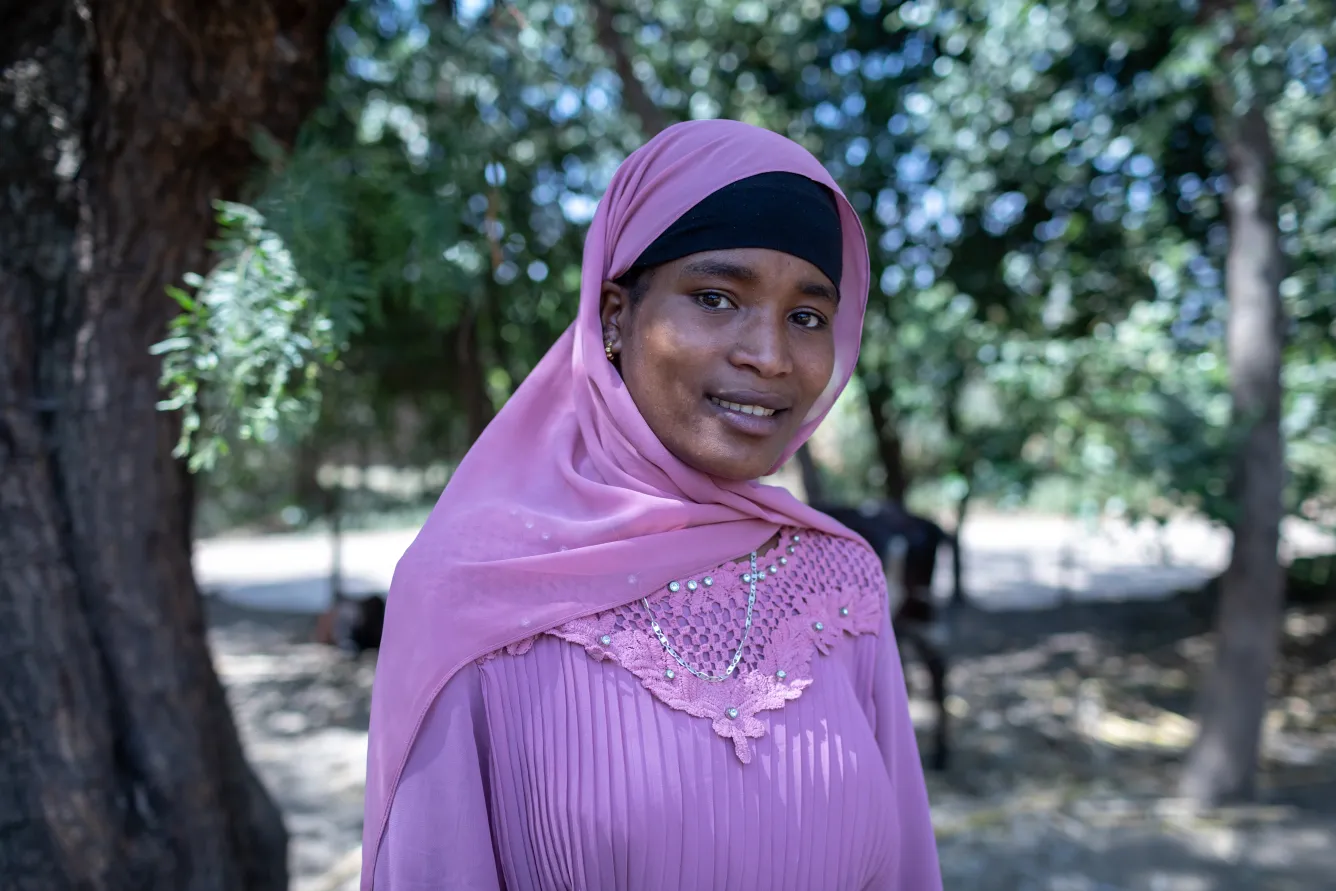 An adolescent girl in pink clothes looks directly at the camera with a slight smile. She is in an outdoor setting.