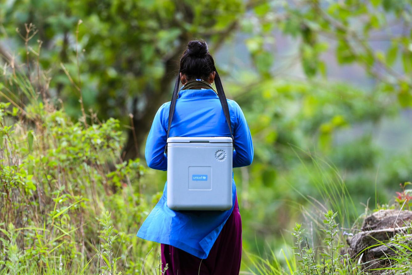 A health worker with a vaccine carrier en route to a community outreach session to vaccinate children under the routine vaccination programme.
