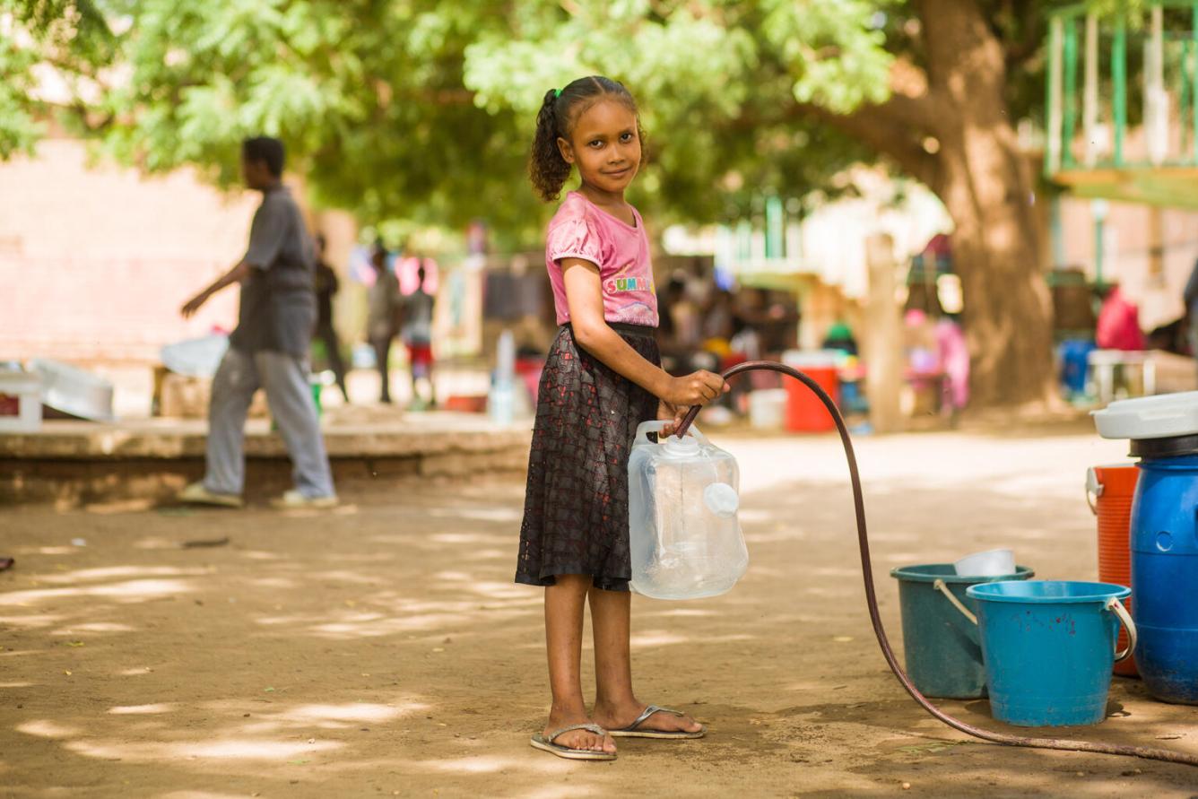 Une fille sourit à l’objectif en faisant le plein d’eau à un point de rassemblement au Soudan.