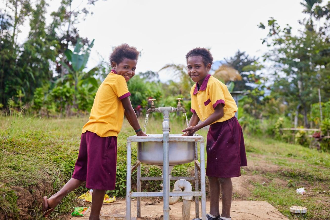 Deux enfants sourient à l’objectif en se lavant les mains à un lavabo extérieur en Papouasie-Nouvelle-Guinée.
