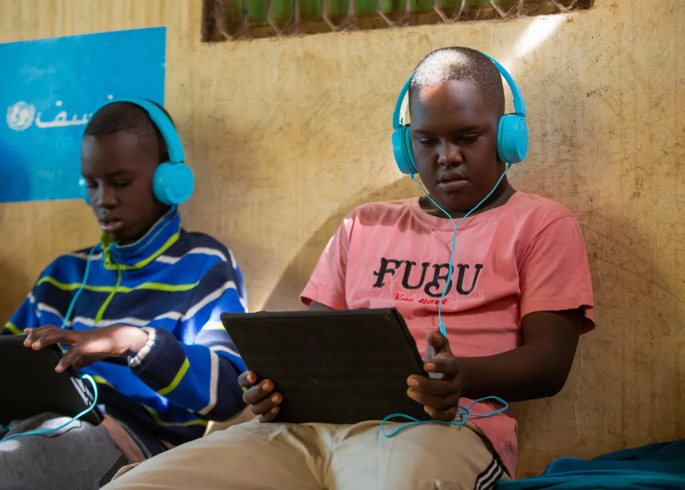 At a UNICEF safe learning space in Sudan, two boys wearing headphones use tablets to learn.