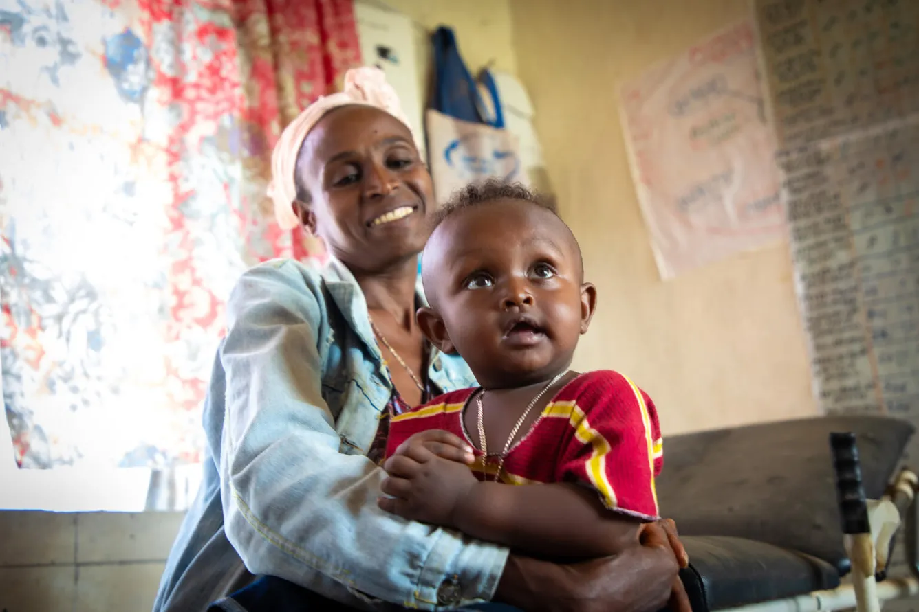 A mother holds her child on her lap, both are smiling.