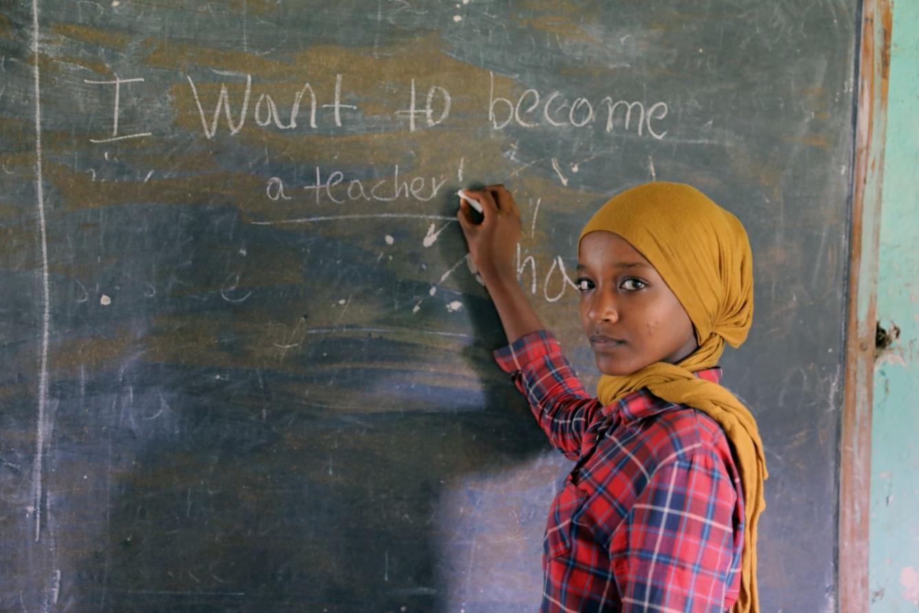 Dans une salle de classe en Éthiopie, la jeune Zemzem, âgée de 13 ans, regarde l’objectif alors qu’elle se tient devant un tableau sur lequel elle a écrit : « Je veux devenir enseignante ».