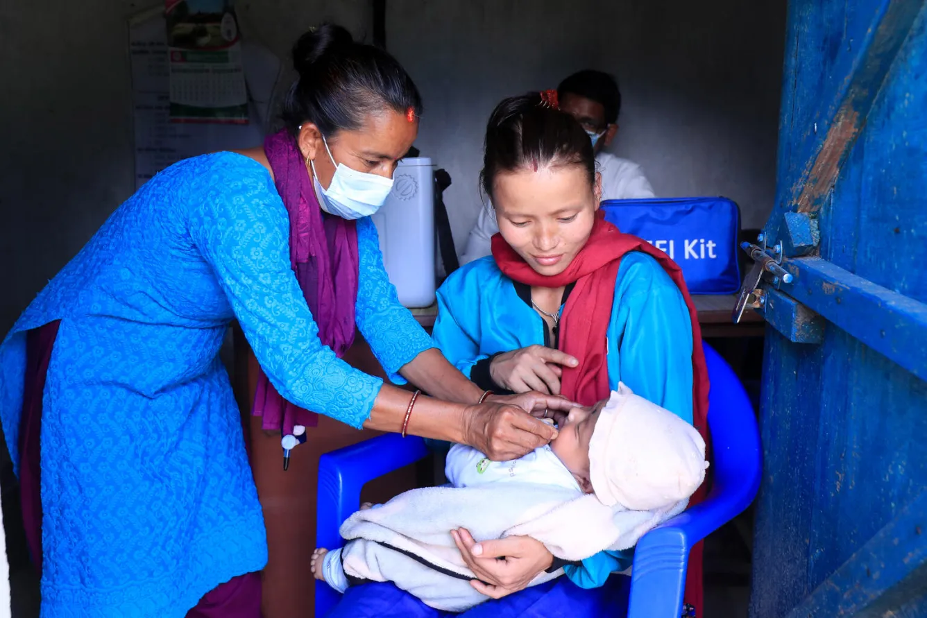 A health worker administers a vaccine to 3-month-old Rhythm, being held by her mother.