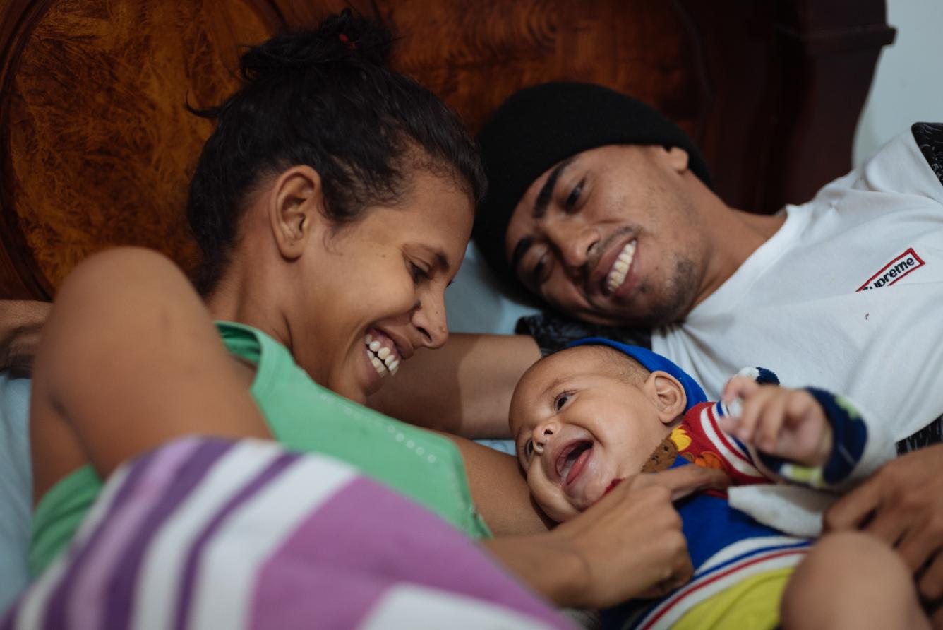 A man and woman peacefully lying on a bed, cradling their baby between them, showcasing a moment of family intimacy.