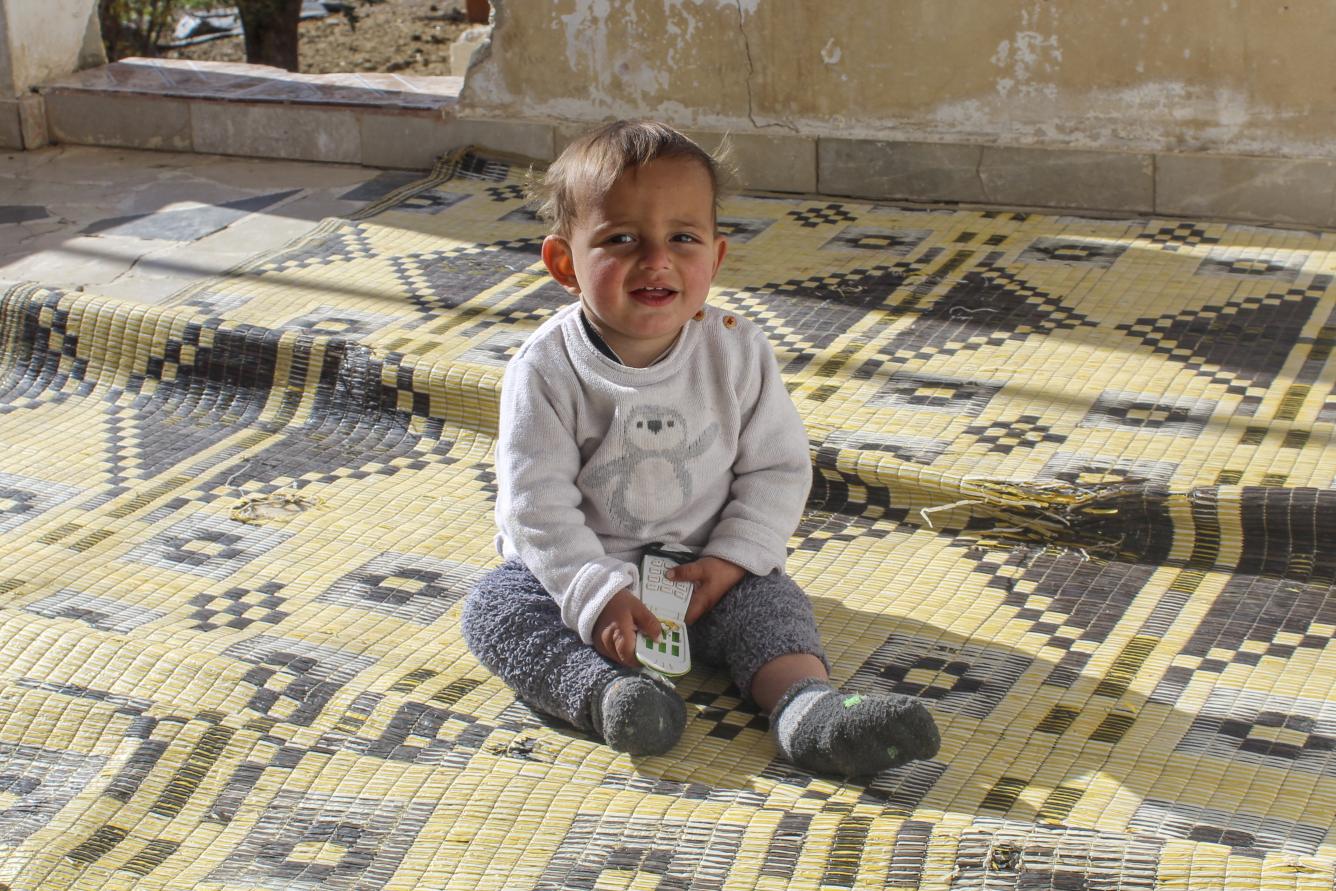One-year-old Morei sits on a carpet in the yard of his home in Obada village, Rural Damascus, Syria