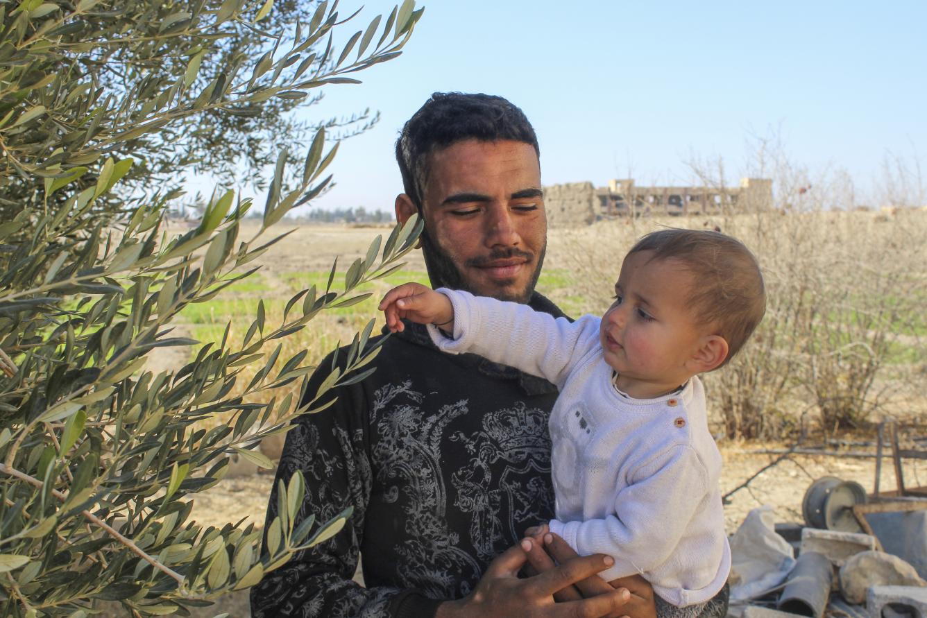 Mohamed, Morei’s father, holds his one-year-old son in the yard of their home in Obada village, Rural Damascus, Syria.