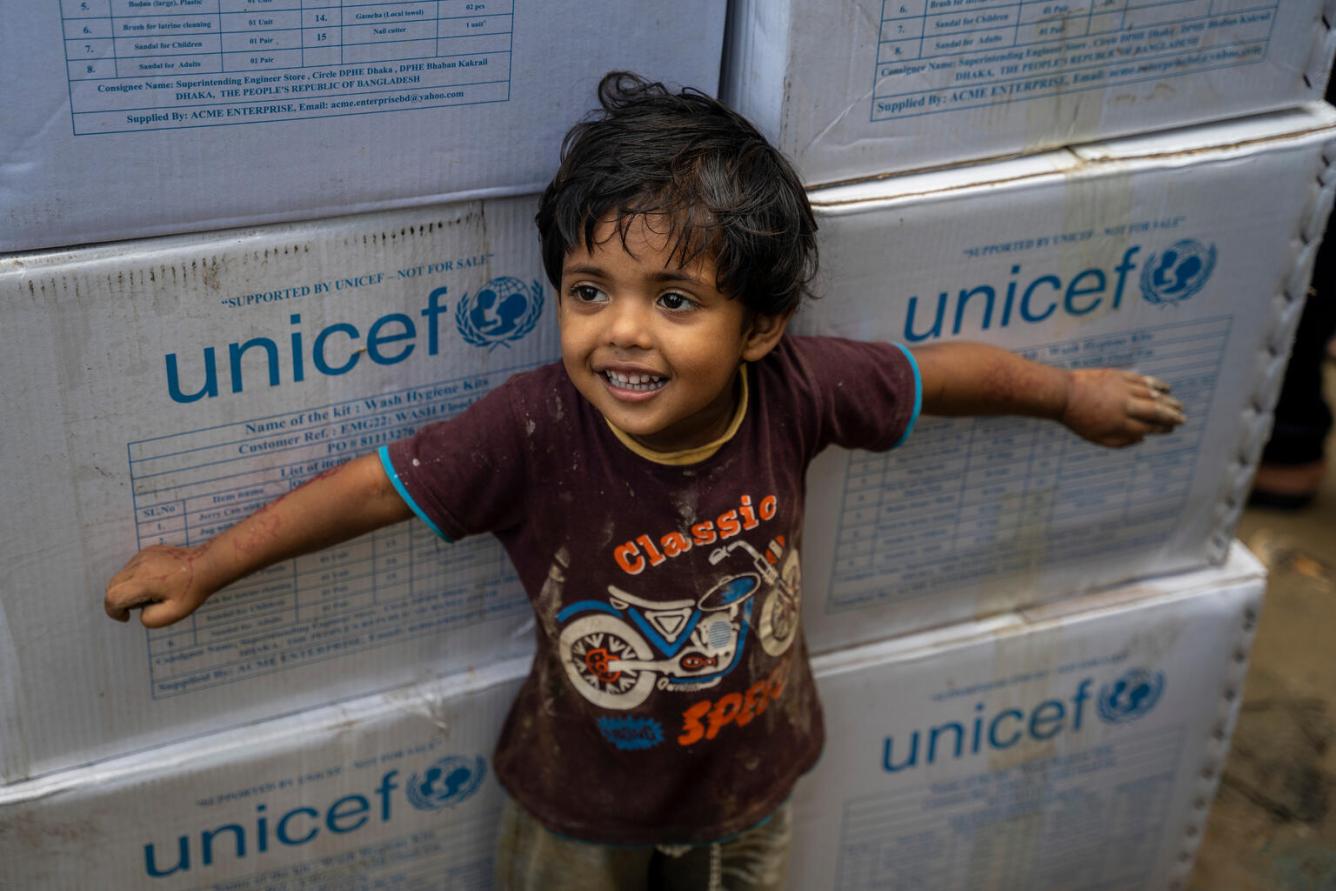 A child stands in front of white UNICEF boxes.