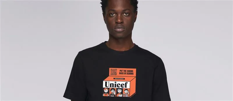 A person wearing the UNICEF X Kotn shirt with a vintage orange UNICEF box design on it.