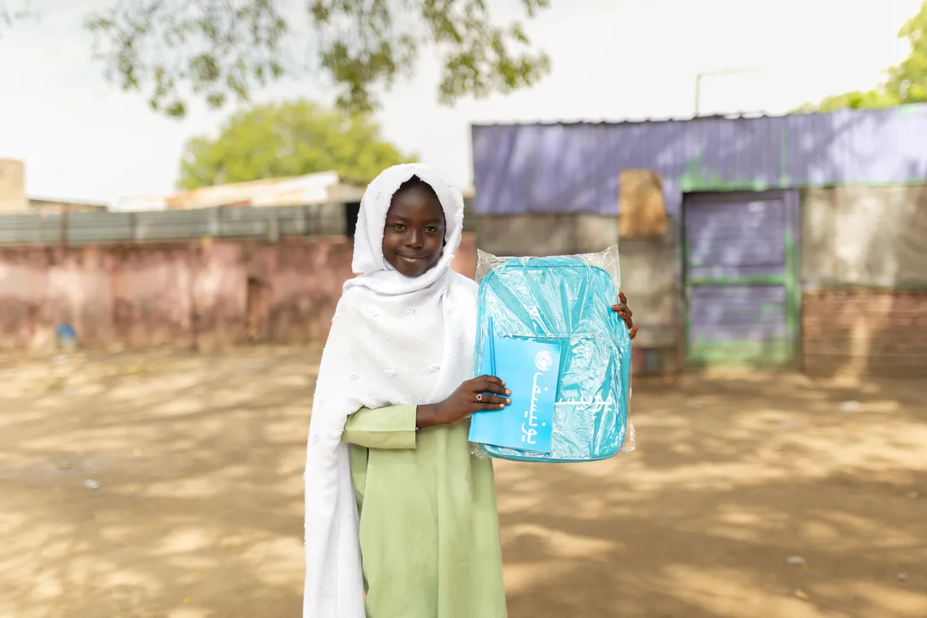 A girl holds up her blue UNICEF backpack and notebook. 
