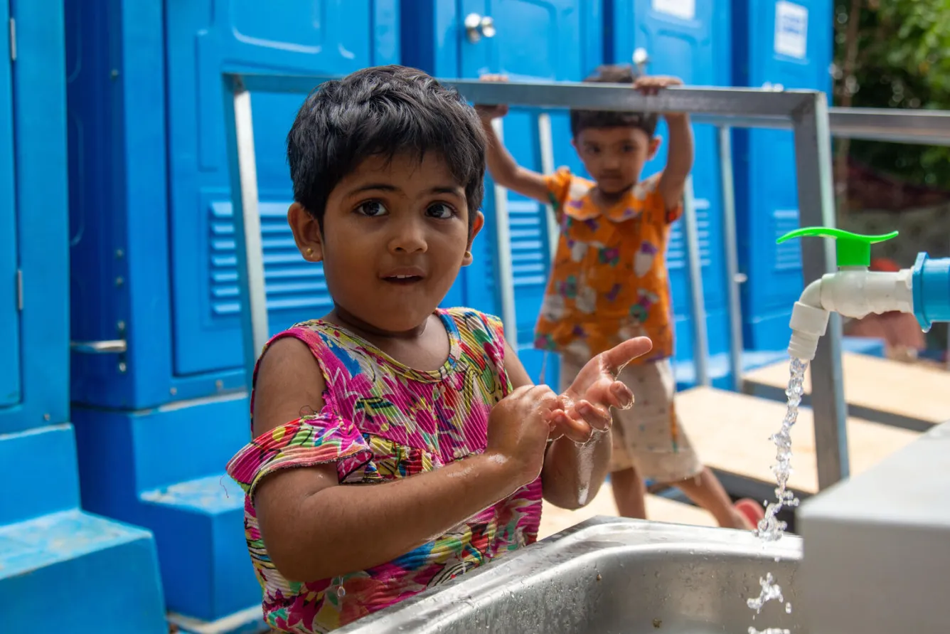A young girl washes her hands at an outdoor tap.  