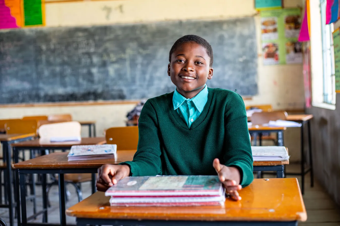 Princess, 14 ans, est assise à son pupitre dans sa salle de classe au Zimbabwe et sourit à l’objectif. 