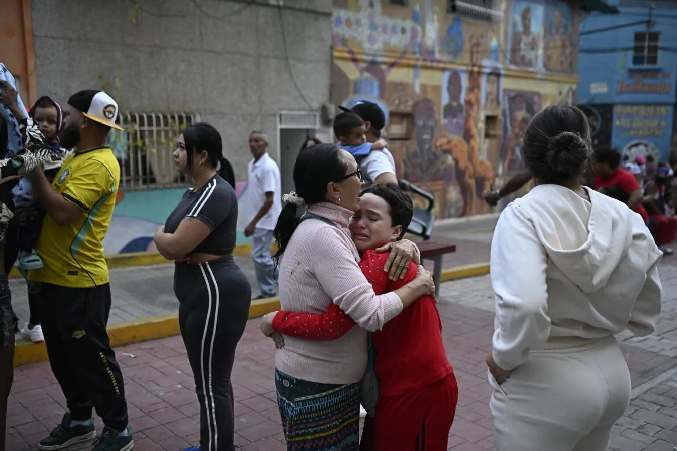 A woman hugs a crying child in the foreground while others stand or hold children nearby.