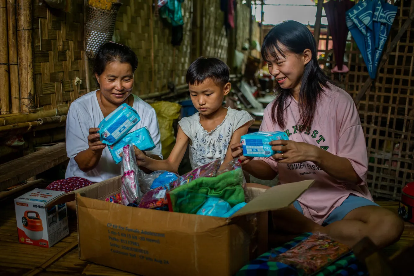 Three people unpack a UNICEF child protection kit in a temporary shelter. 