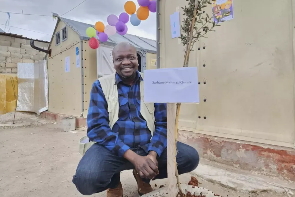 An adult sitting in an outdoor location by a posted sign that says Sarhane Mahmat Khamis.