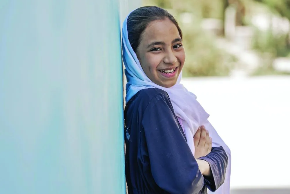 Sur la photo, Sadaf, onze ans, sourit à la caméra à sa droite, les bras croisés, alors qu'elle s'appuie contre le mur extérieur du bâtiment de son école.