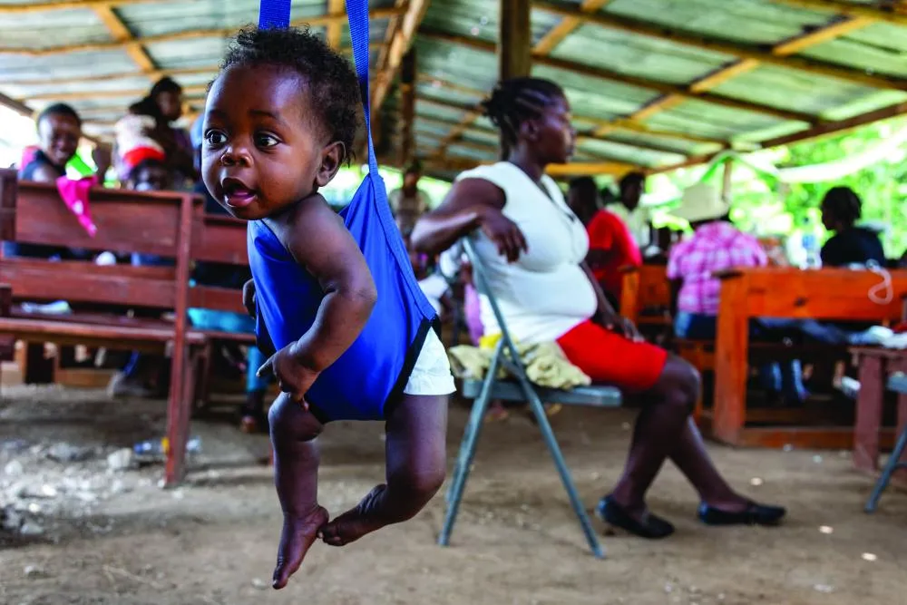 Fredlyne, six mois, est photographiée en train de sourire alors qu'elle est assise sur le siège en tissu d'une balance, ses pieds pendant au-dessus du sol, dans une clinique de santé mobile extérieure.