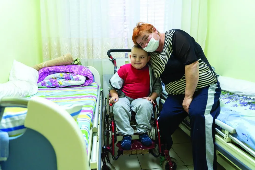 Dans une chambre d'hôpital, Markar, six ans, sourit en s'asseyant sur le siège d'un déambulateur, à côté de sa mère qui sourit également et appuie sa tête contre la sienne.