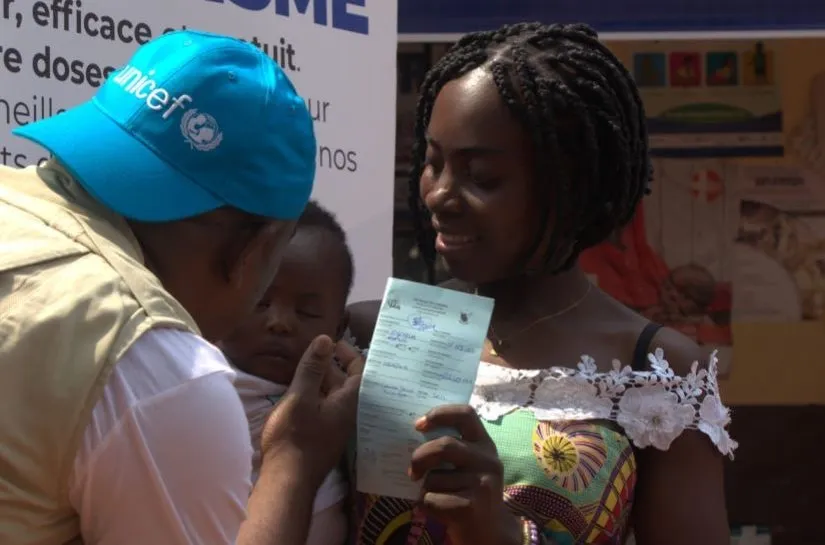 A UNICEF worker interacts with a woman and the baby she is holding at a vaccination clinic.