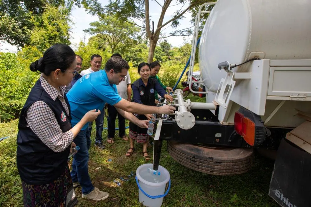 A group of adults operating a water pump attached to a water truck.