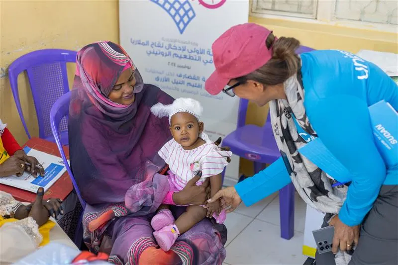 A mother is seated, holding her daughter after receiving malaria vaccine 