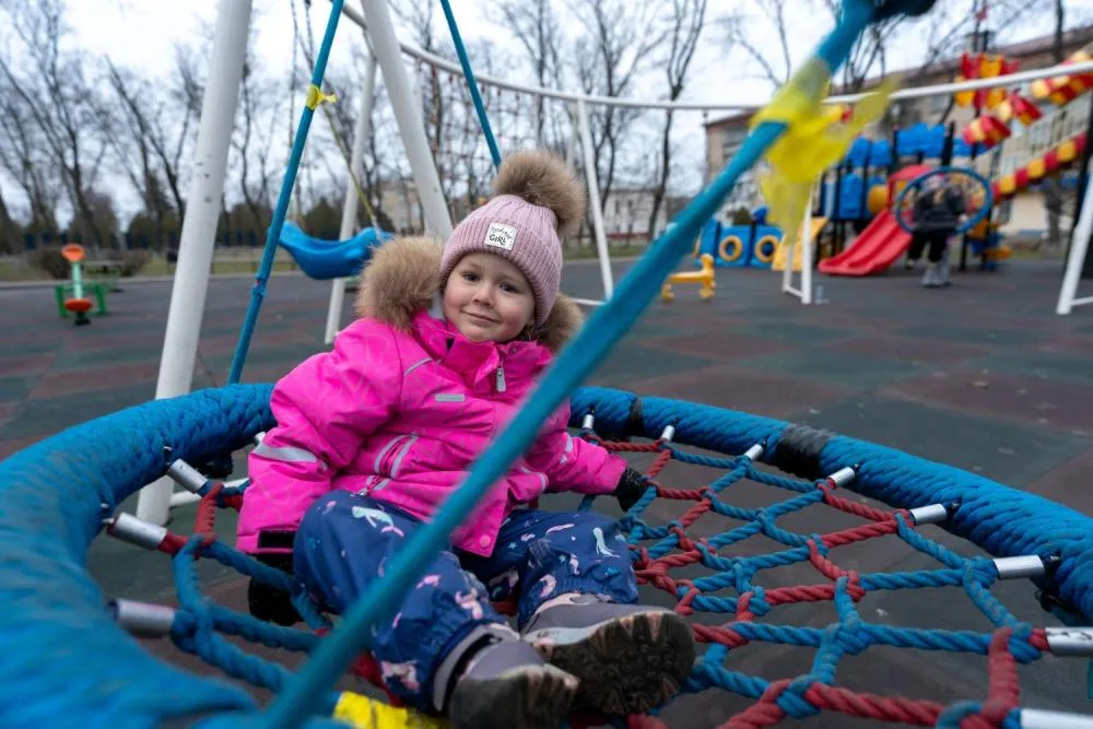 Une fille portant un manteau rose sourit à l’objectif alors qu’elle se balance sur une aire de jeux.