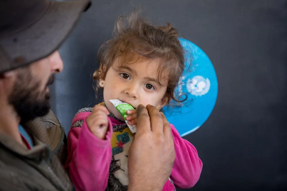 A person helps a child eat from a sachet of therapeutic food.