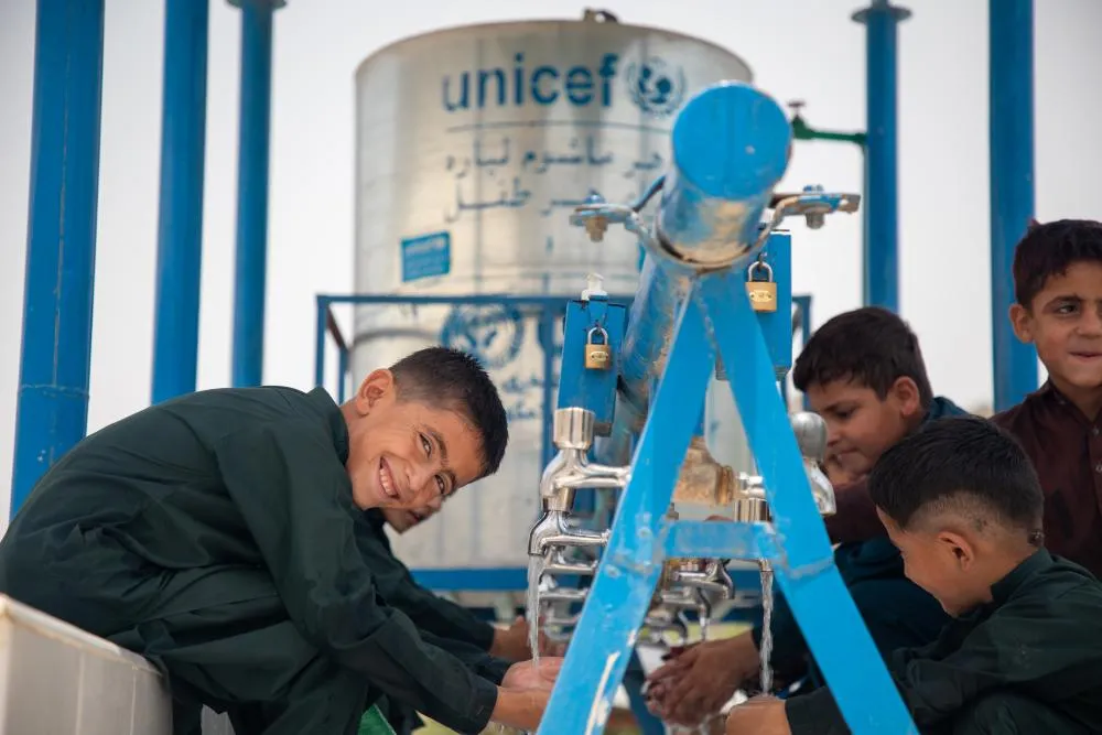 Children smile and wash their hands at an outdoor water tap.